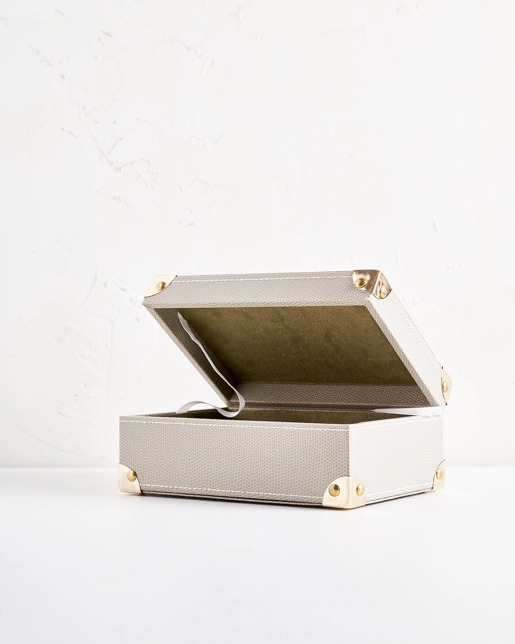 Open light gray jewelry box with gold accents on a white surface and background.