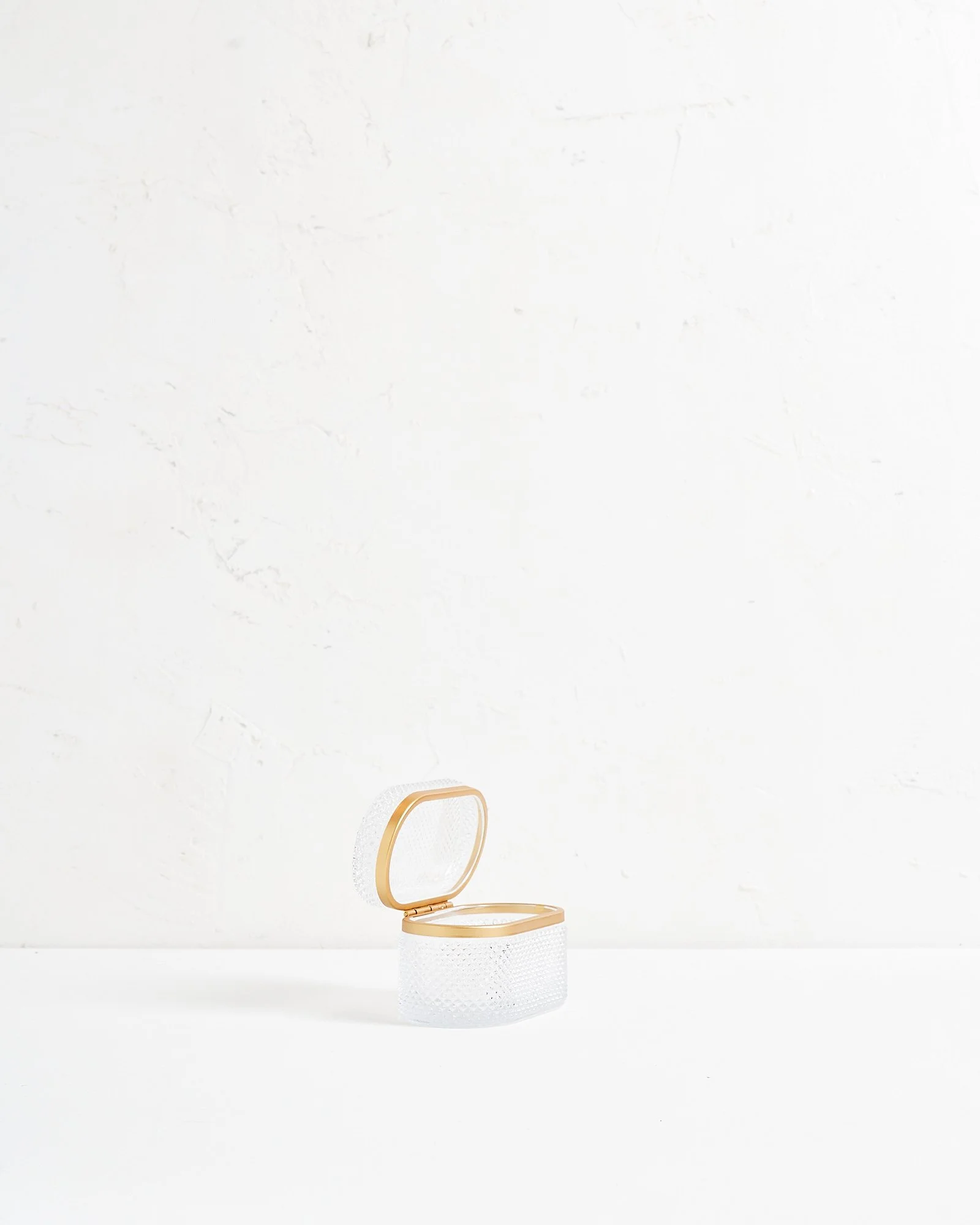 Empty white crystal jewelry box with a gold border near a white wall