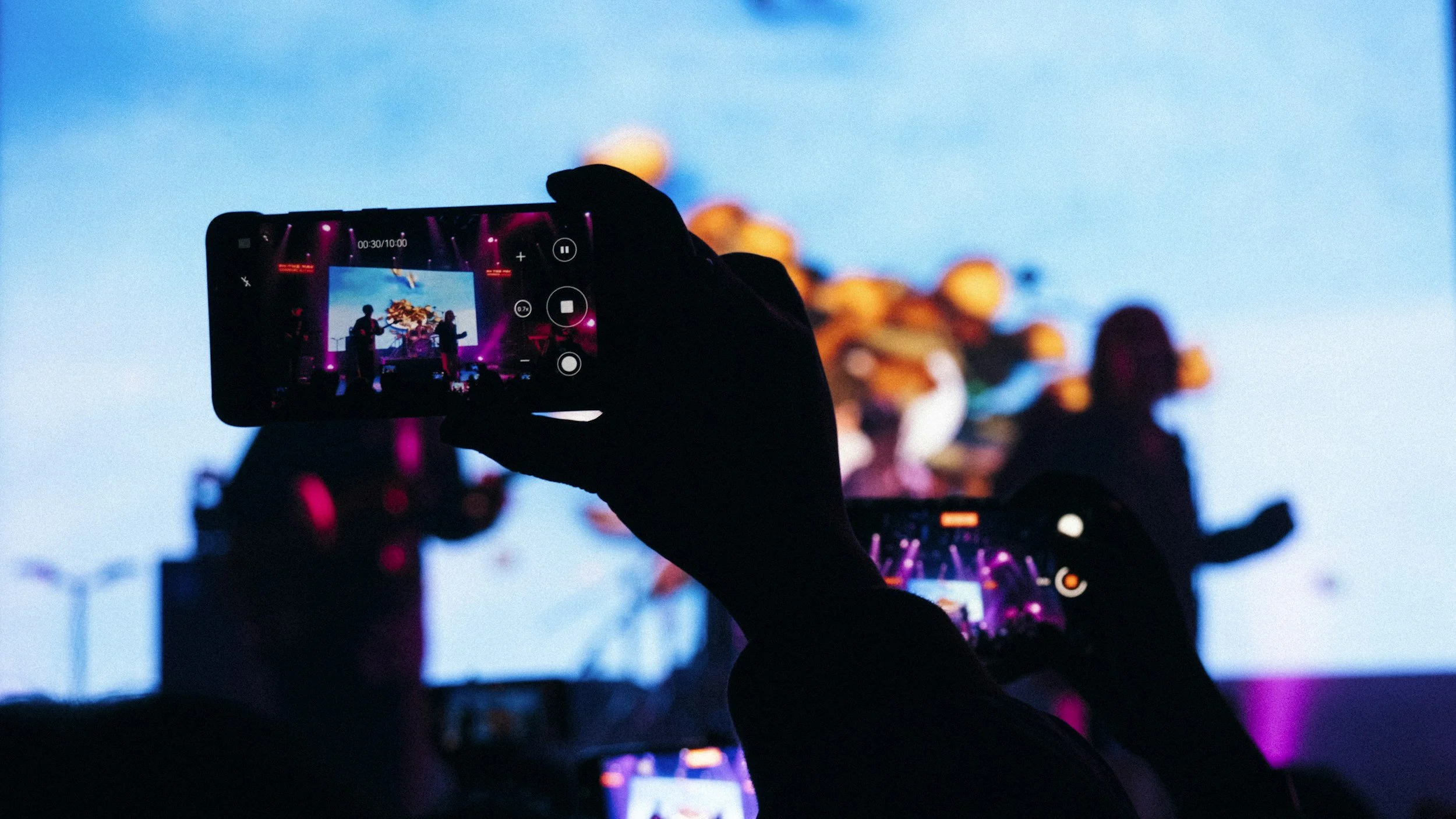 People taking photos or videos of a concert or stage performance with their smartphones in a dark setting.