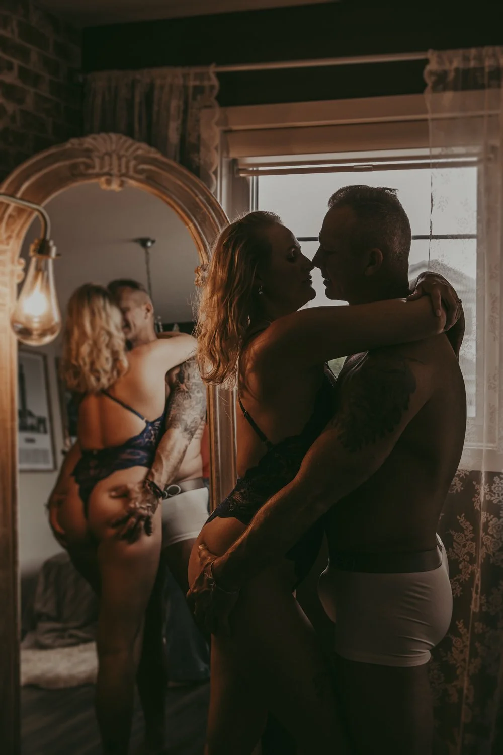 a man and woman standing in front of a mirror posing during a couples boudoir photography session in Edmonton