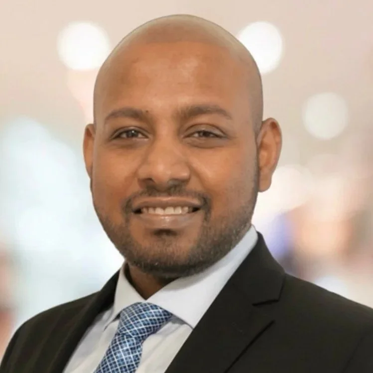 Professional man in a suit smiling, blurred background with lights.