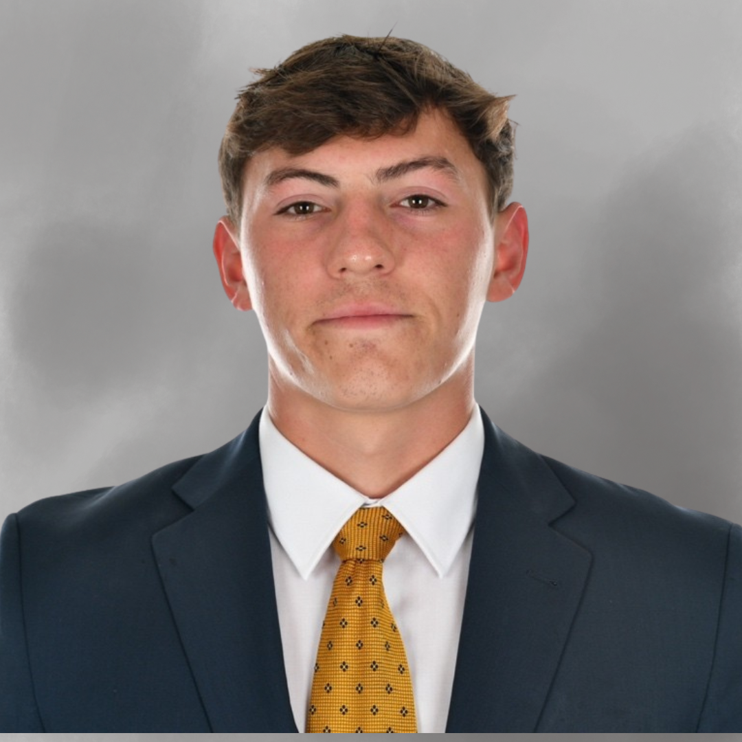 A young man in a formal suit with a yellow tie, posing for a professional headshot against a gray background.