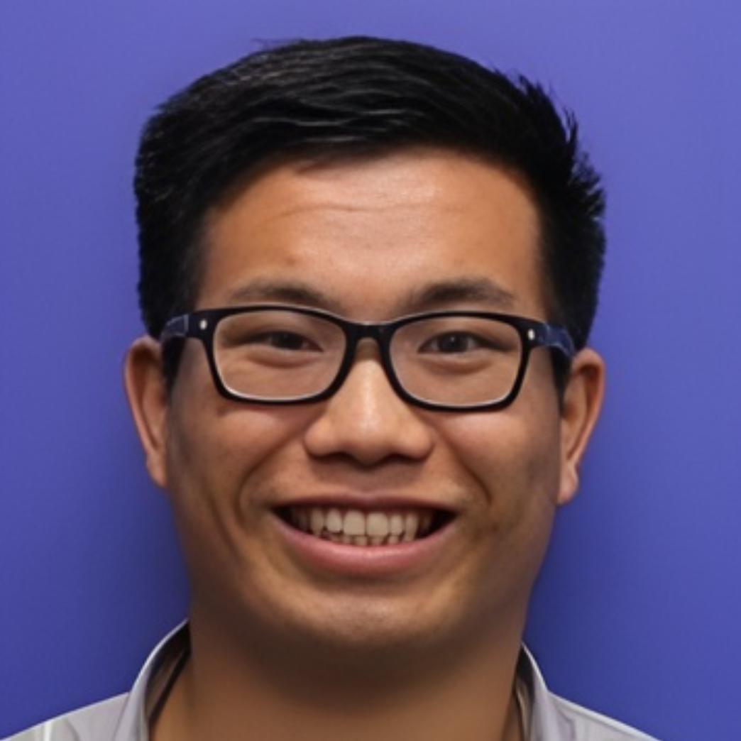 A young man with short black hair, wearing black glasses, smiling, against a blue background.