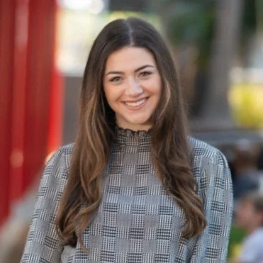 A woman with long brown hair smiling outdoors