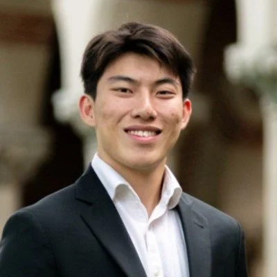 A young man in a suit smiling outdoors.