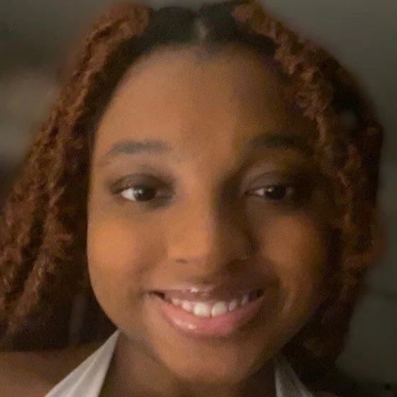 Close-up of a young woman with curly hair smiling and showing her teeth.