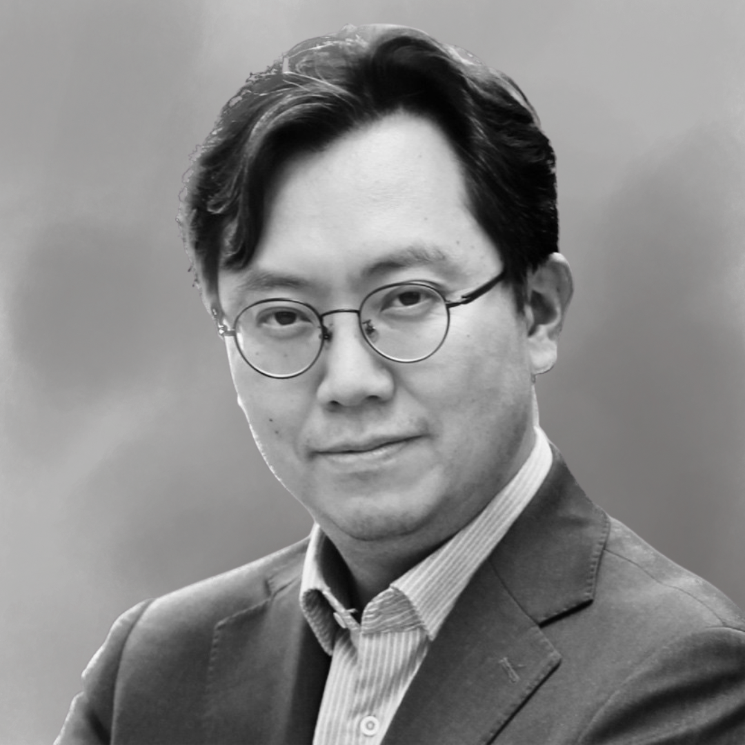 Black and white portrait of a man wearing glasses, a collared shirt, and a blazer, looking directly at the camera.