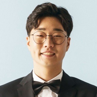 A young man with curly hair and glasses, wearing a tuxedo and bow tie, smiling at the camera.