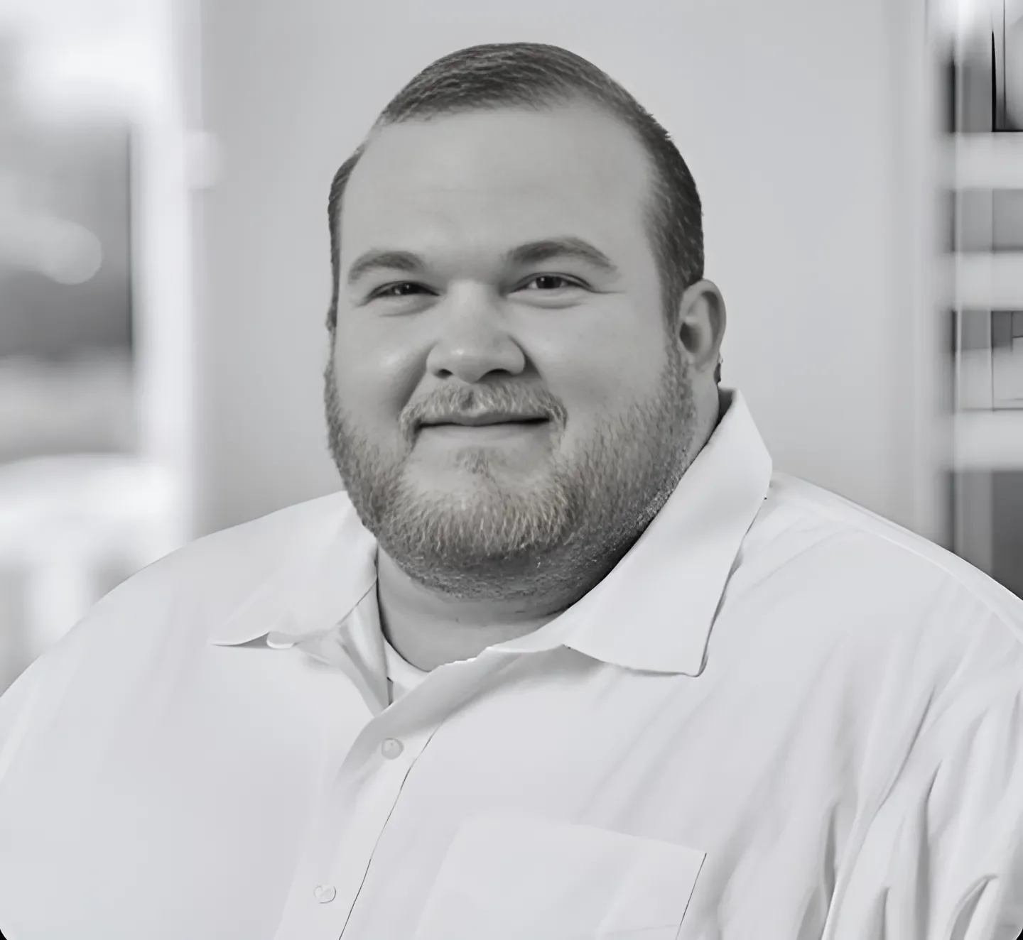 Black and white portrait of a man with short hair and a beard, wearing a collared shirt, smiling at the camera.