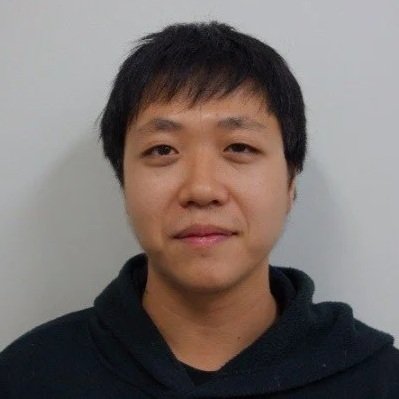 A young Asian man with short black hair, wearing a black hoodie, standing against a light gray background.