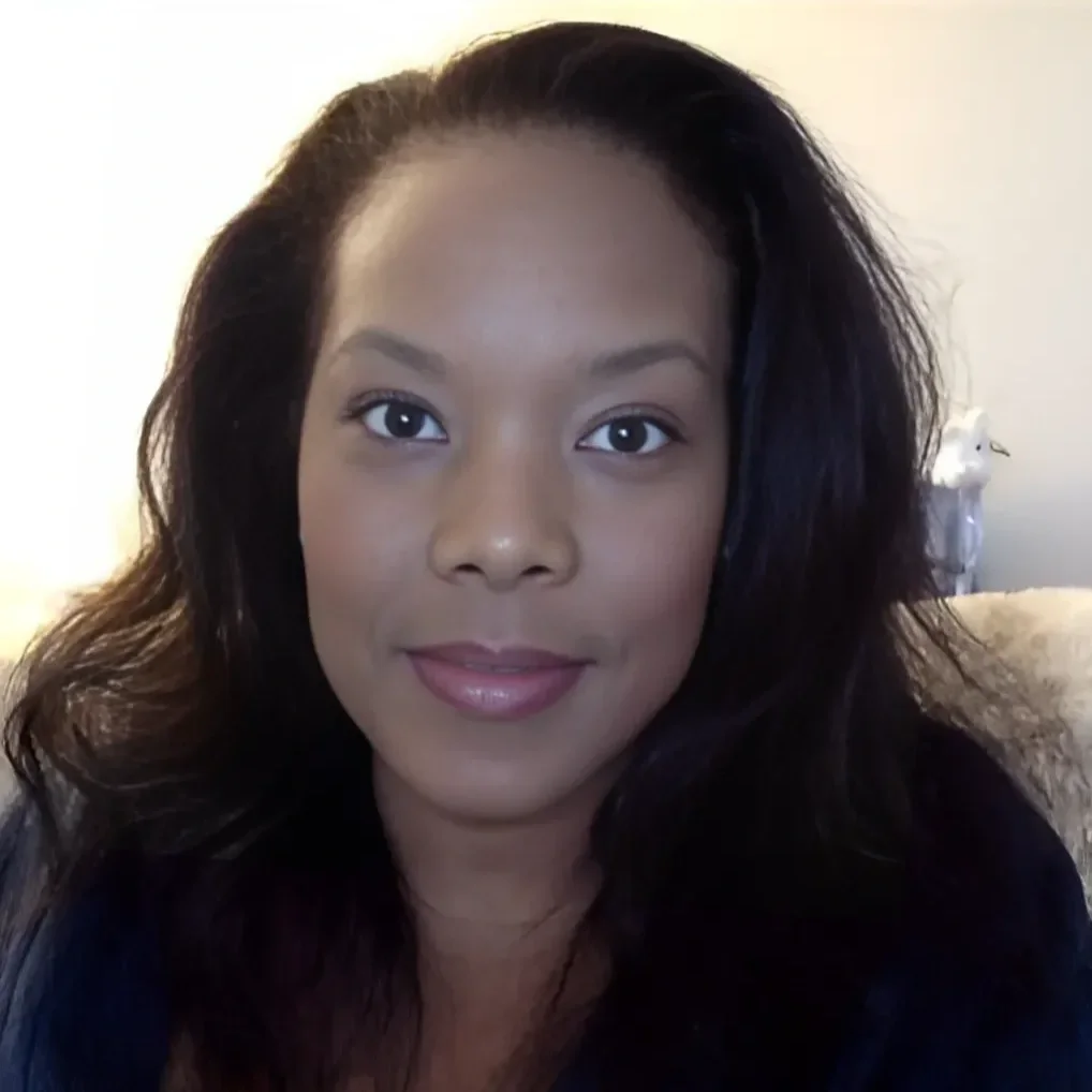 Portrait of a woman with dark, wavy hair and a subtle smile, indoors with a blurred background.