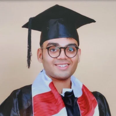 Young man in graduation cap and gown with glasses smiling at the camera.