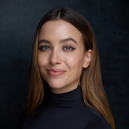 A young woman with long brown hair, wearing a black turtleneck, smiling softly against a dark background.