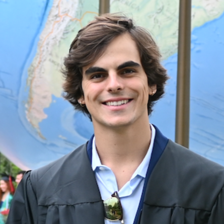A young man with brown hair smiling in front of a map of South America at a graduation ceremony.
