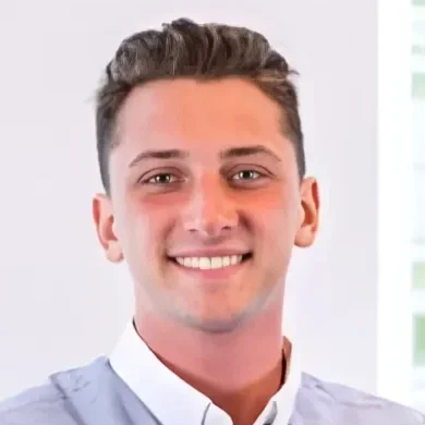 A young man with short brown hair smiling, wearing a light-colored shirt.