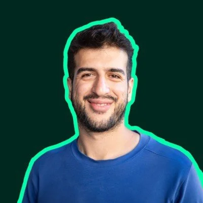 A smiling man with dark hair and beard, wearing a blue shirt, outlined with a neon glow against a dark background.