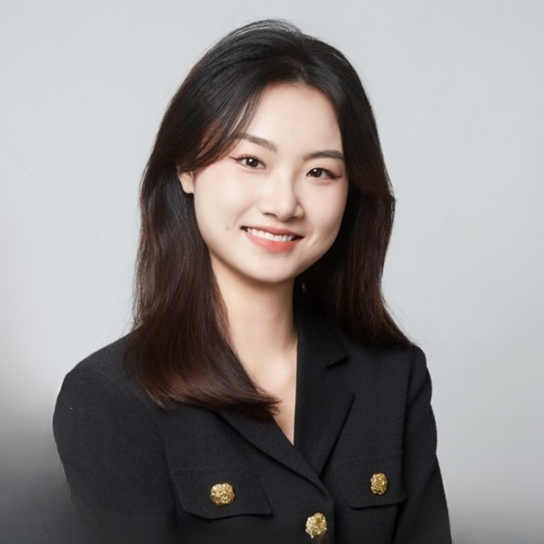Headshot of a young woman with dark brown hair, smiling, wearing a black blazer with gold buttons, against a plain light gray background.