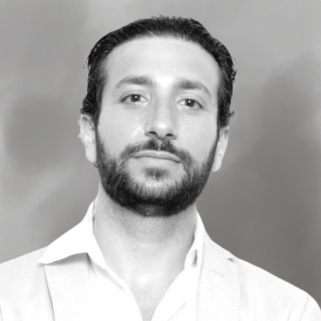 Black and white portrait of a man with dark, slicked-back hair, a beard, and wearing a collared shirt.