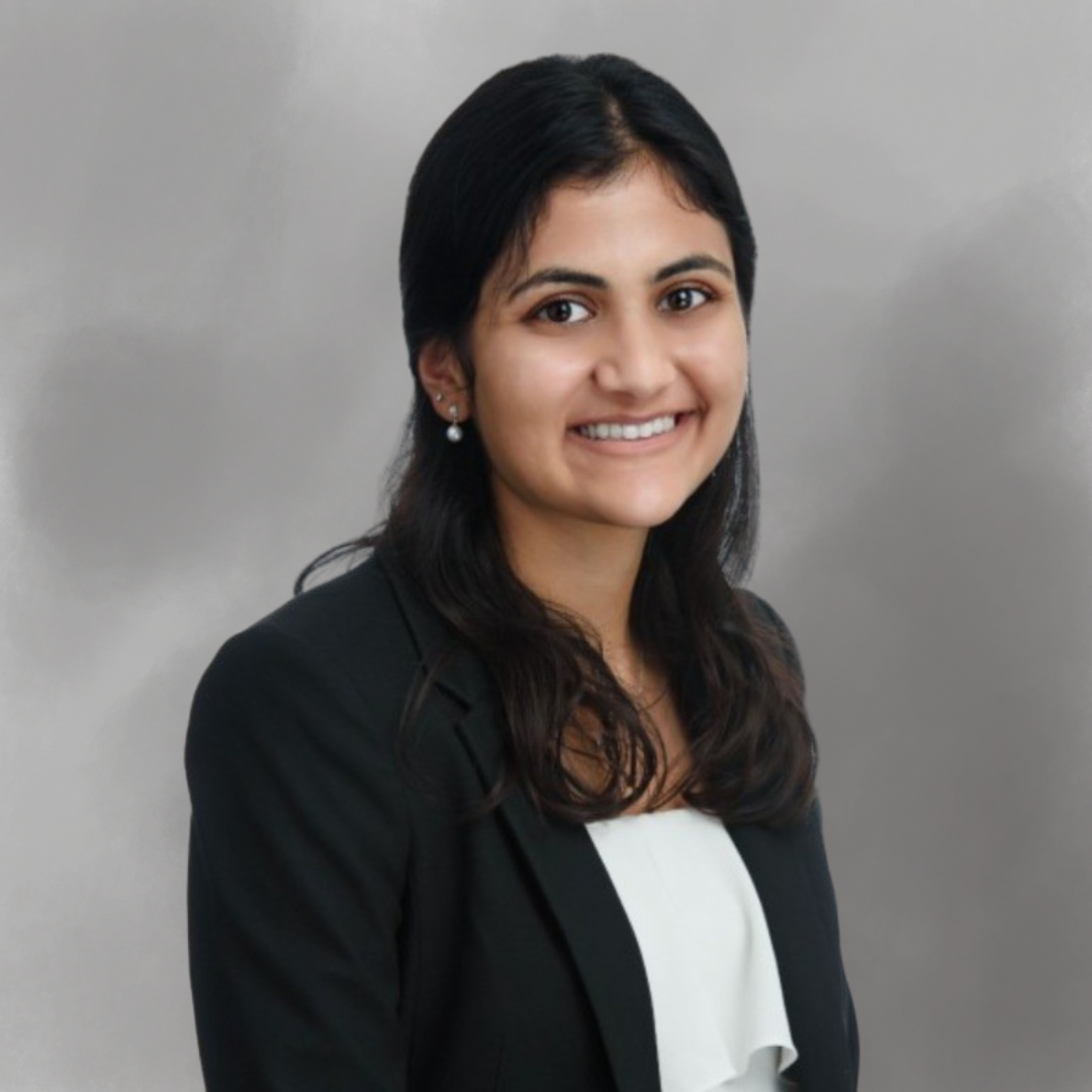 A woman with dark hair, wearing a black blazer and white top, smiling at the camera.
