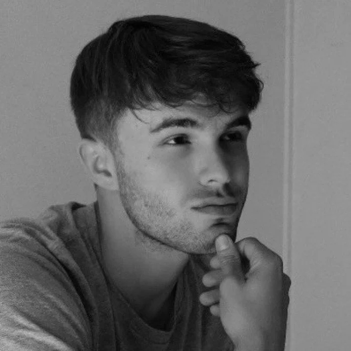 Black and white photo of a young man with short, dark hair, resting his chin on his hand, looking thoughtfully to the side.