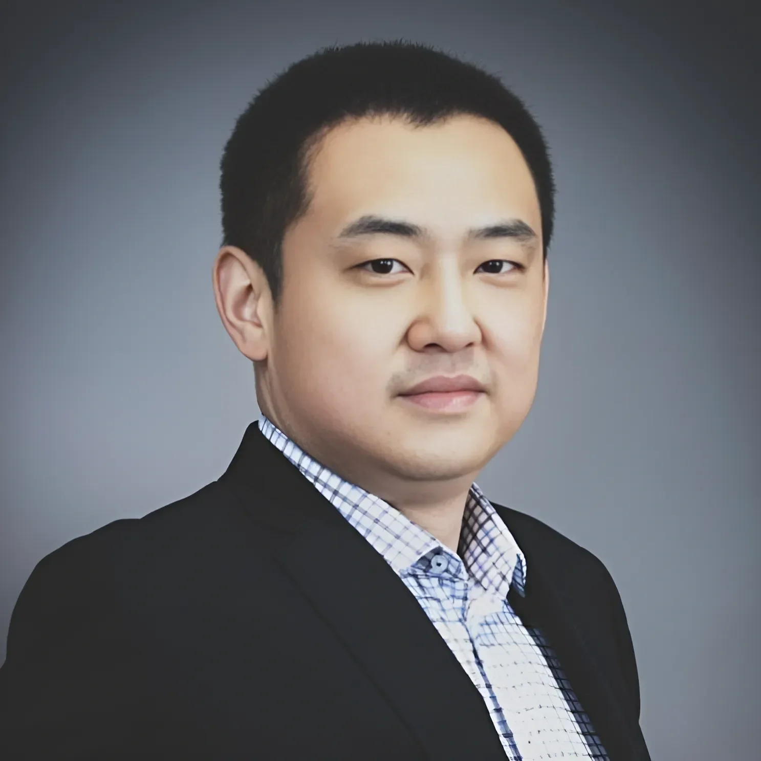 Professional headshot of a young Asian man in a black suit jacket and checkered shirt, against a gray background.