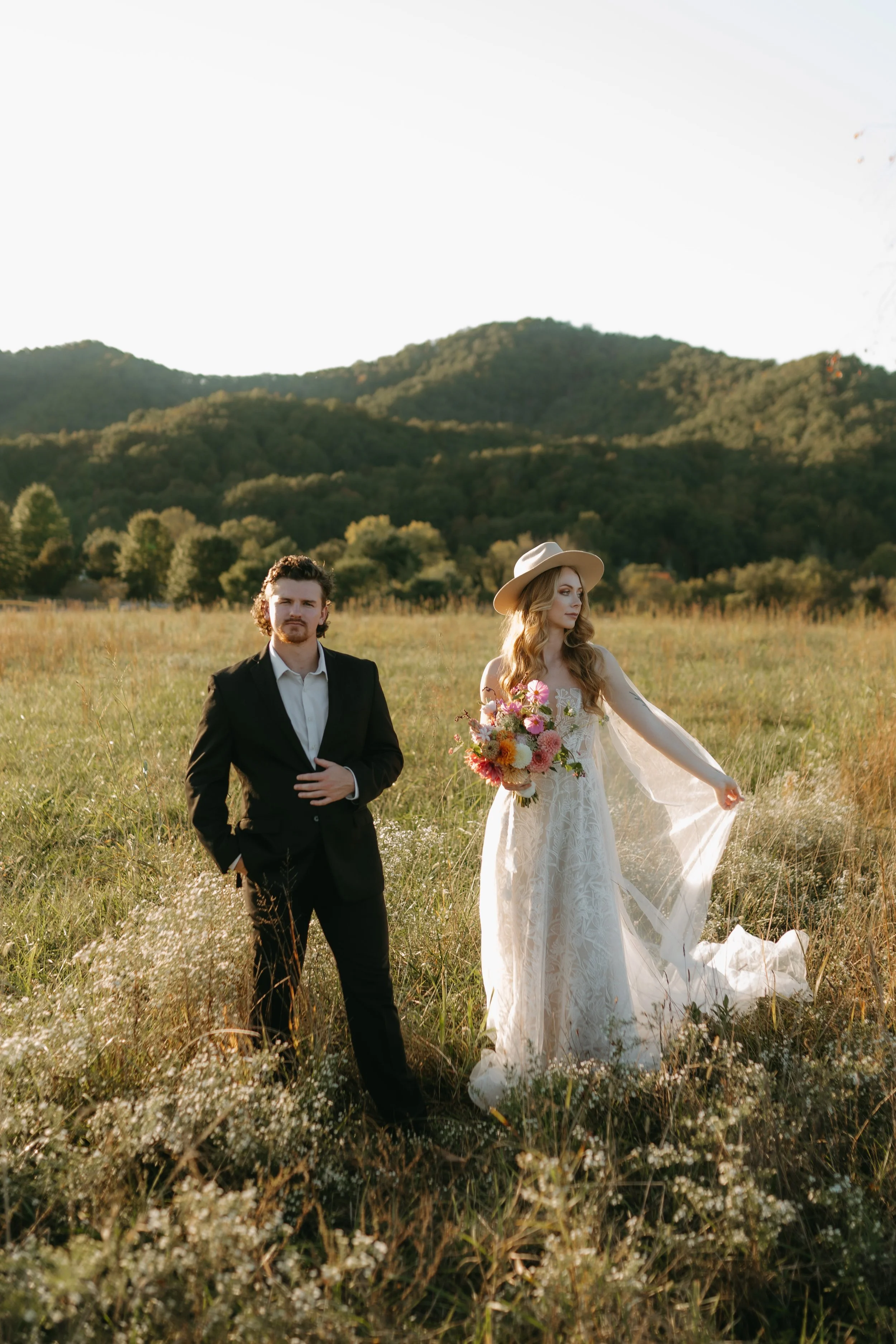 Bride and groom in a meadow in East Tennessee. Bride wearing hat and veil and holding a bouquet of dahlias and tuberose.