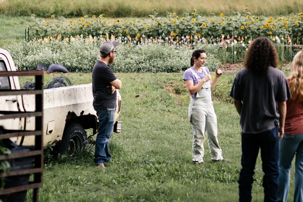 Flower-farmer greets group in front of rows of flowers for cutting and rustic pickup truck.