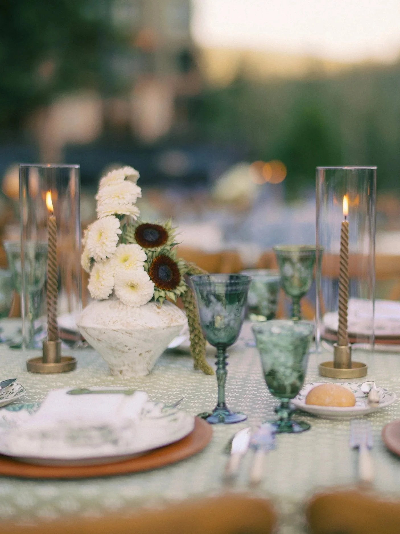 Elegant outdoor dining table with floral centerpiece, candles, and glassware at sunset.