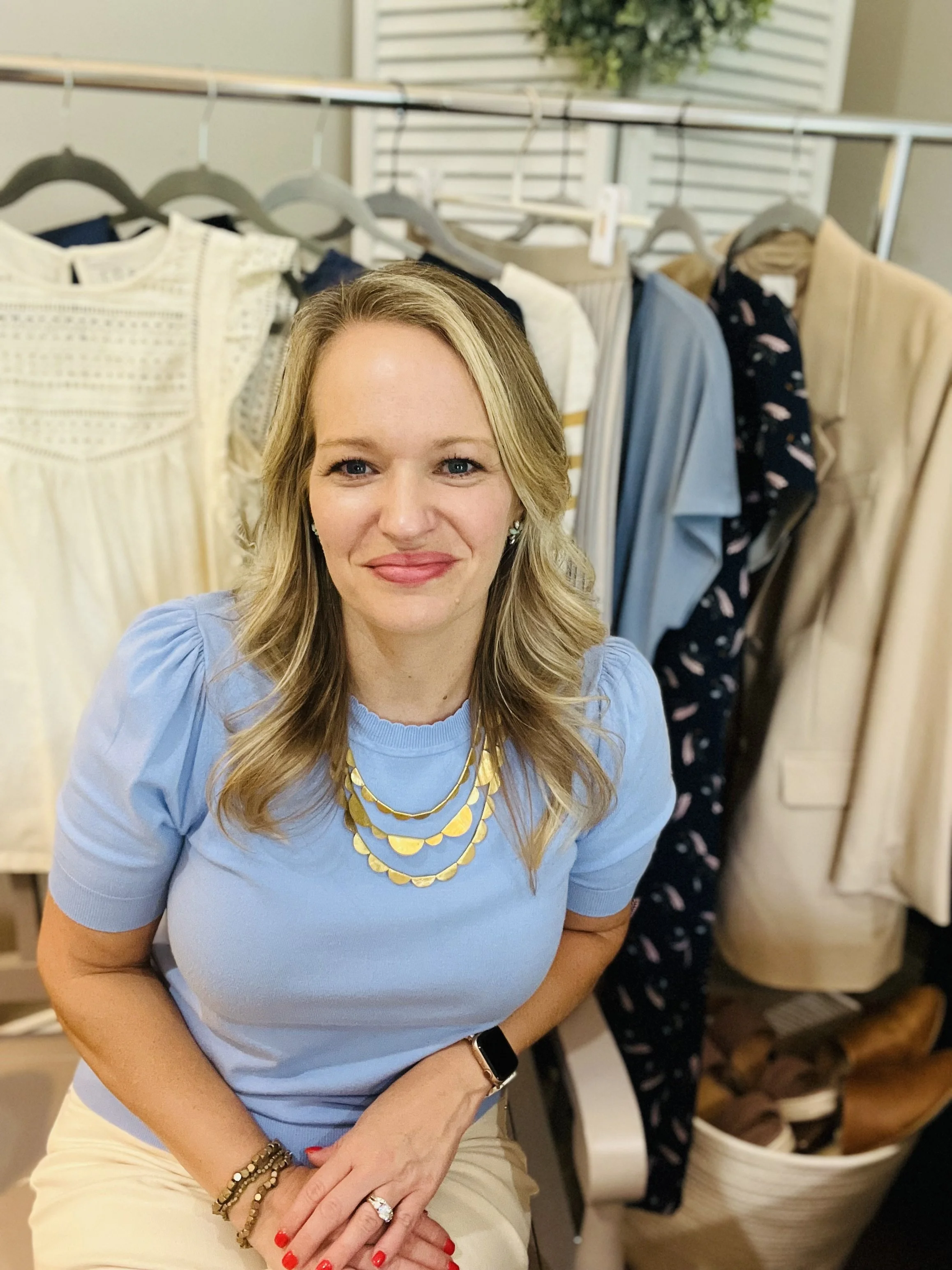 San Antonio stylist Laura Longmire sits in front of rack of women's clothing smiling at camera