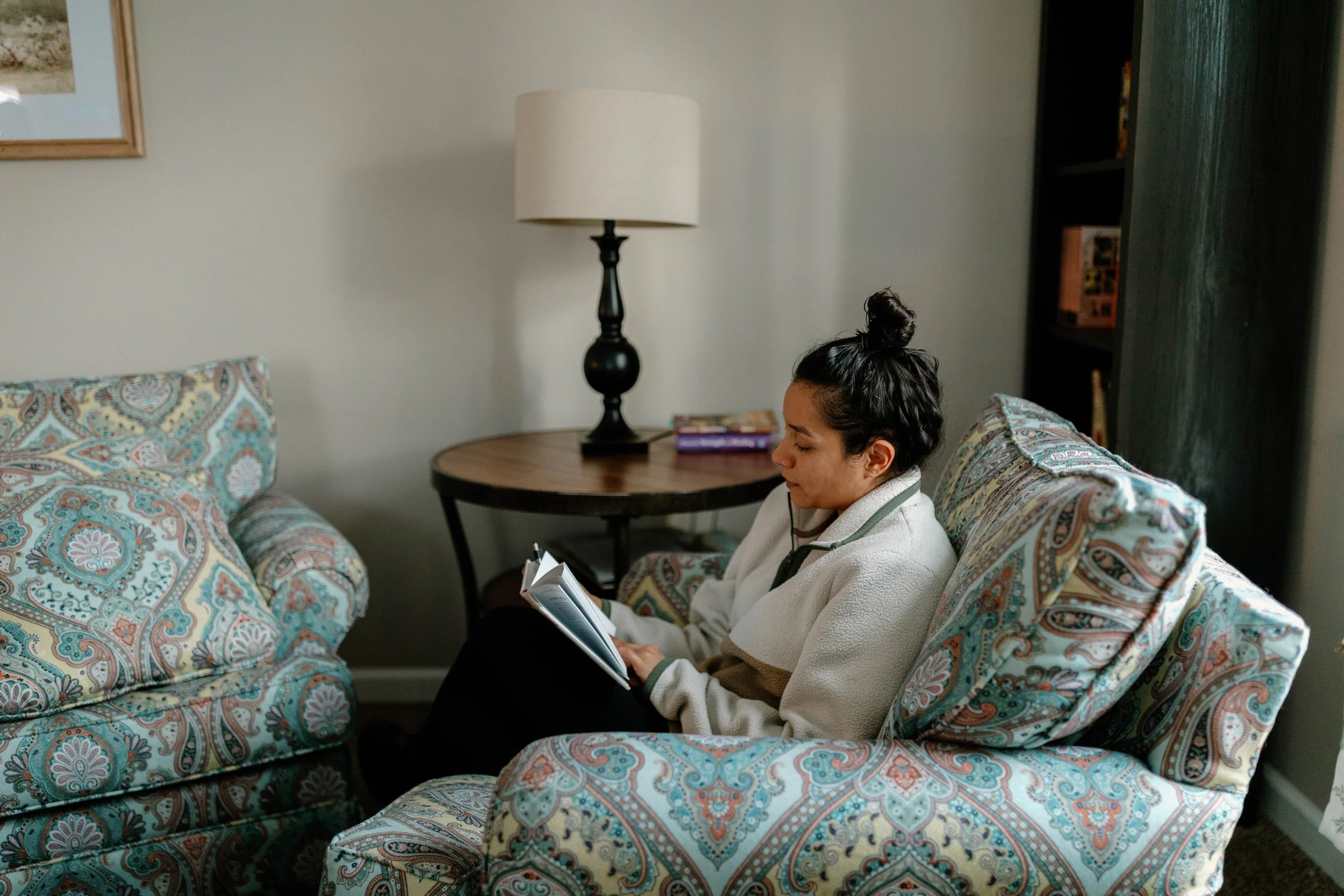A woman sitting on a gray and turquoise patterned couch reading a book.