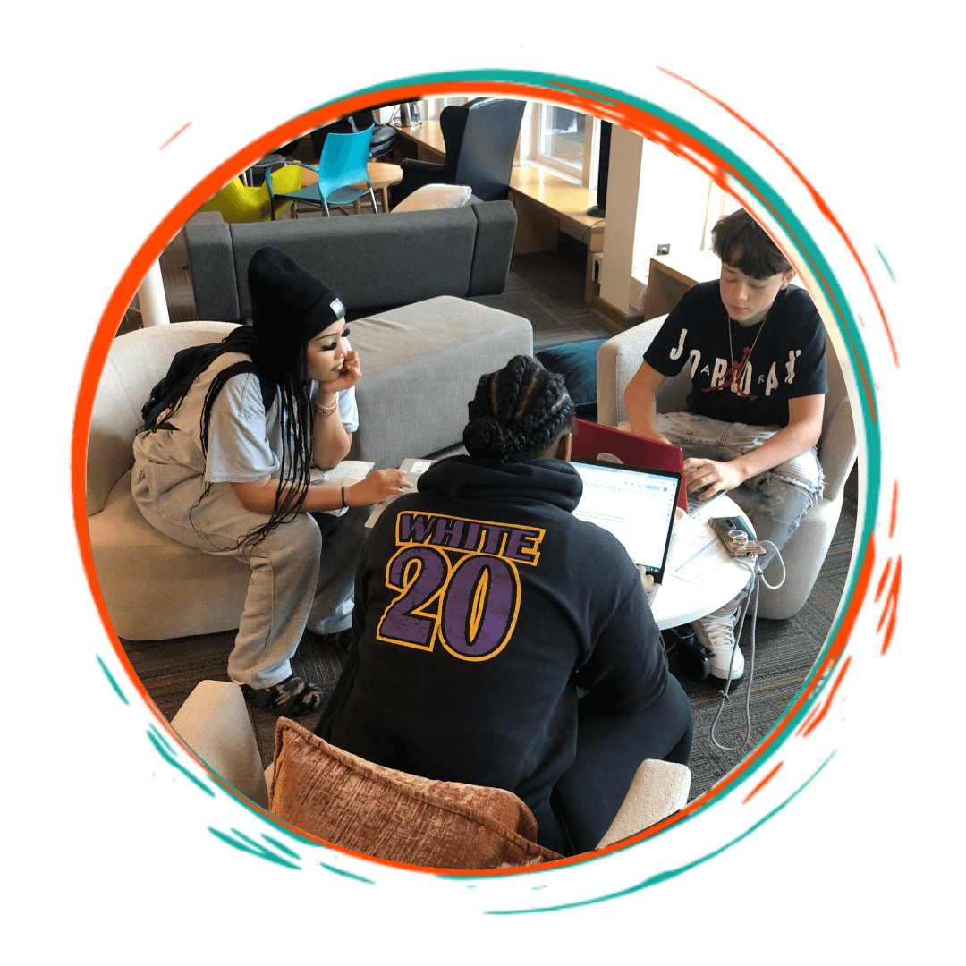 Three young people working on laptops and tablets together in a cozy indoor setting with couches and chairs.