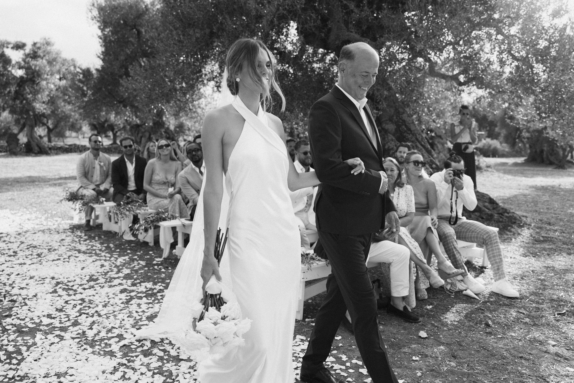  this modern bride walking down the aisle with her father in a simple silk wedding gown and low bun styled with pearl stud earrings by abellie. 