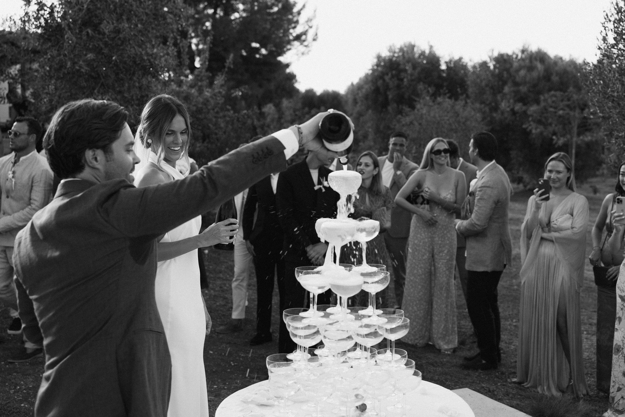 a modern and cool bride and groom pouring a champagne tower at their wedding reception in italy.