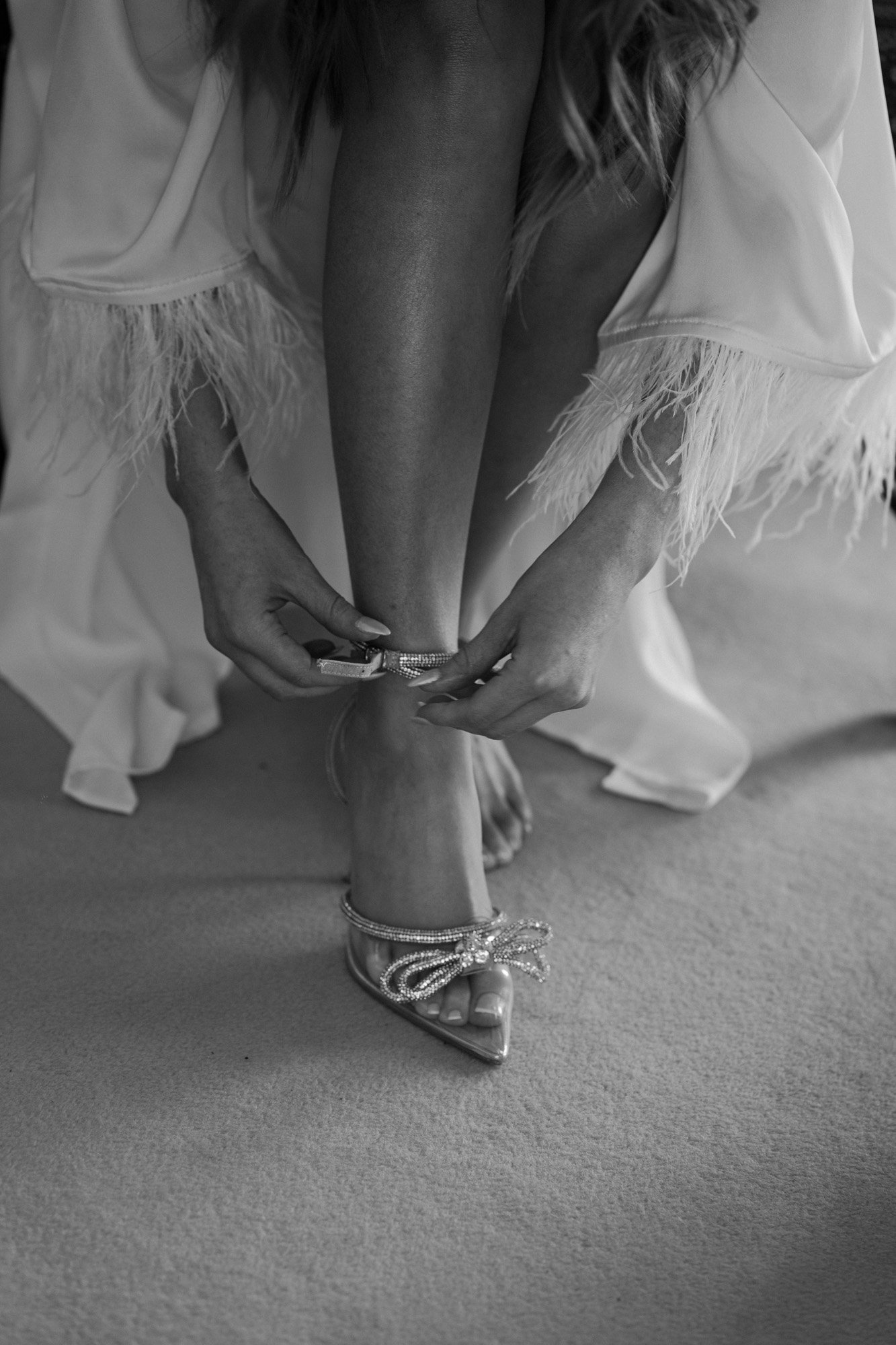  the bride putting on her bridal billini shoes in a classic getting ready black and white photo. 