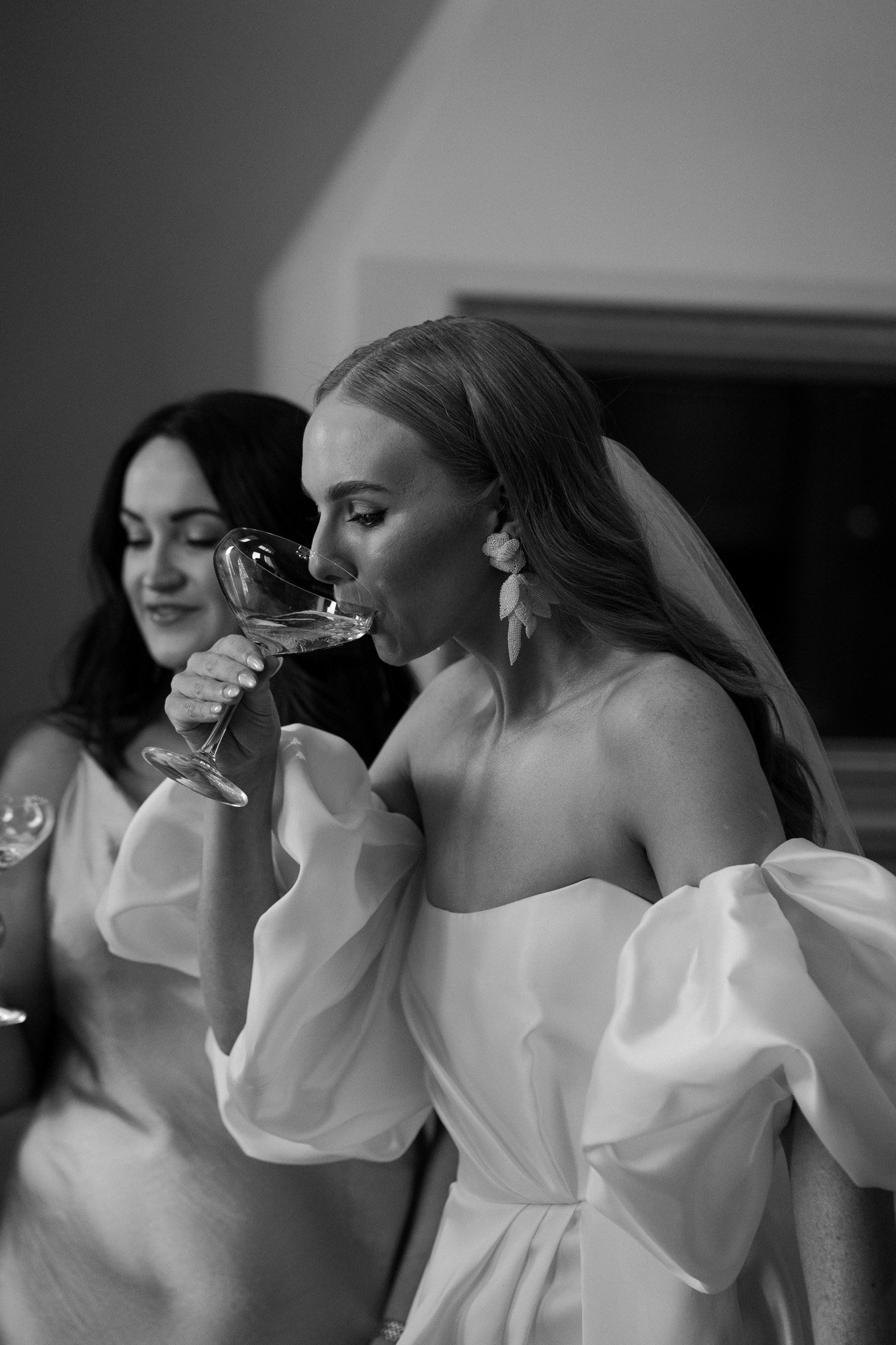 the bride drinking champage as she gets ready in her silk ball gown by alena leena and ab ellie maj drop earrings.