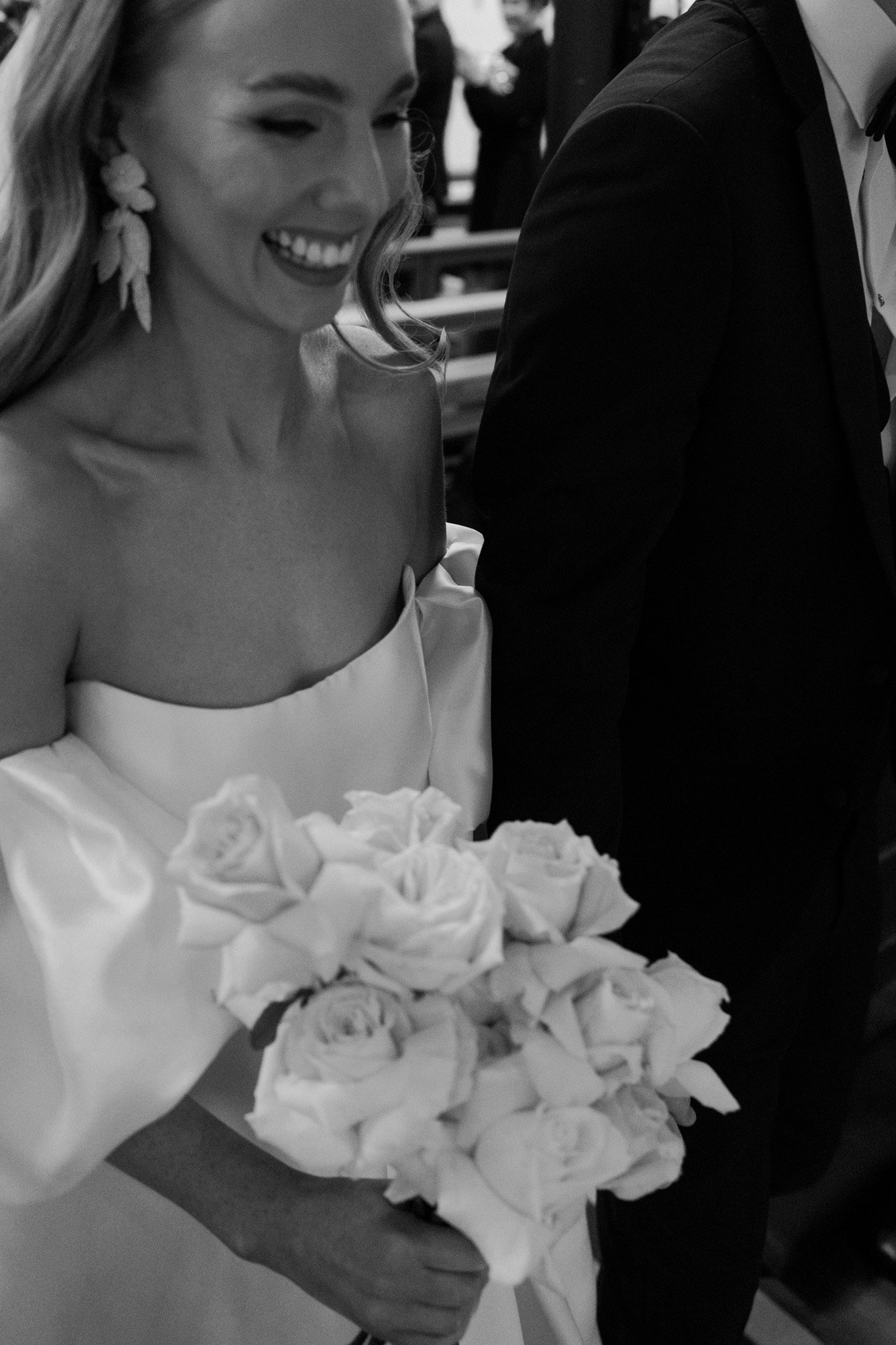 a happy bride holding her bouquet and walking into her wedding ceremony in a classic black and white photo.