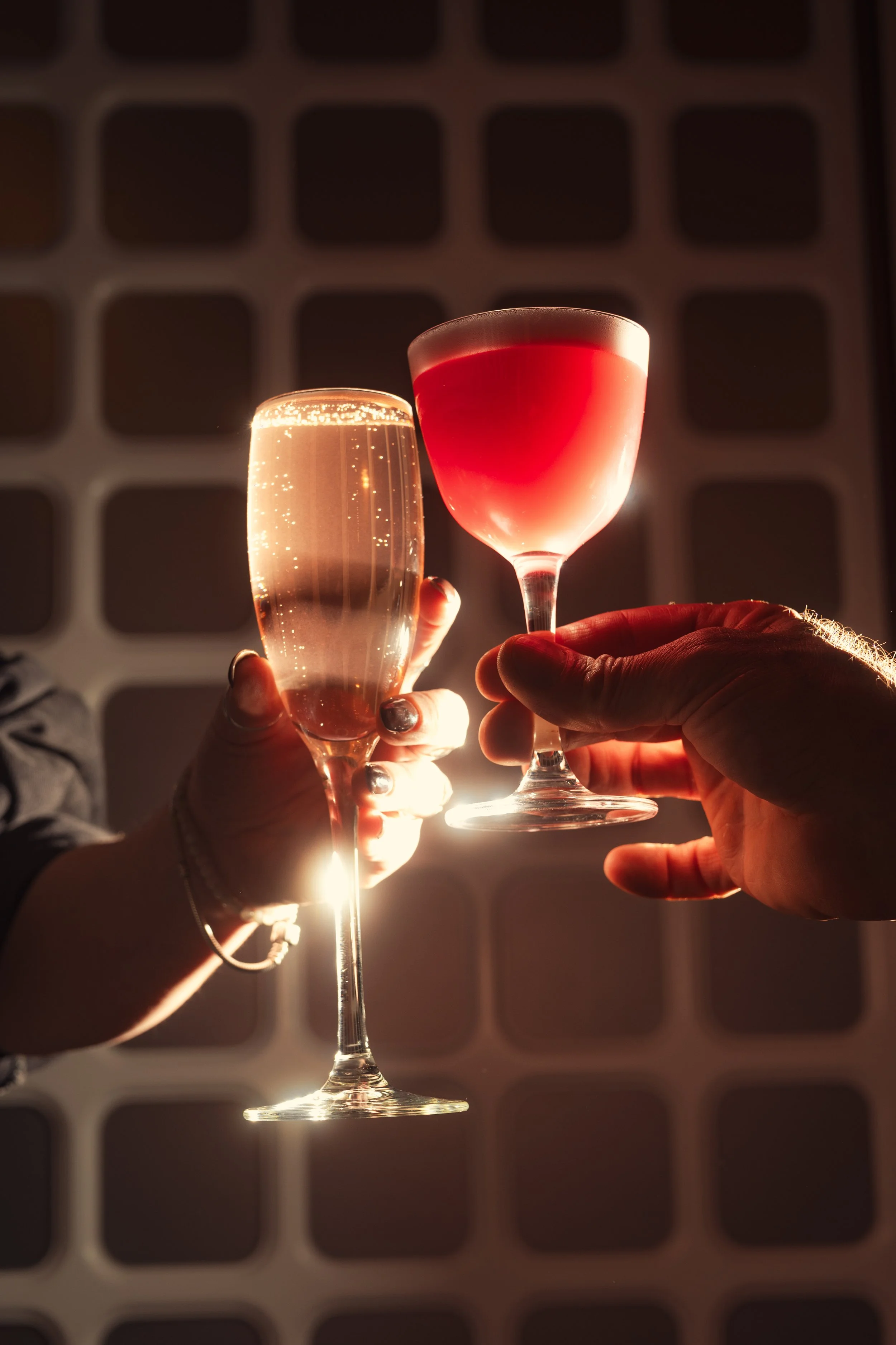 Two people clinking glasses of champagne and wine, backlit with warm lighting, celebrating indoors.