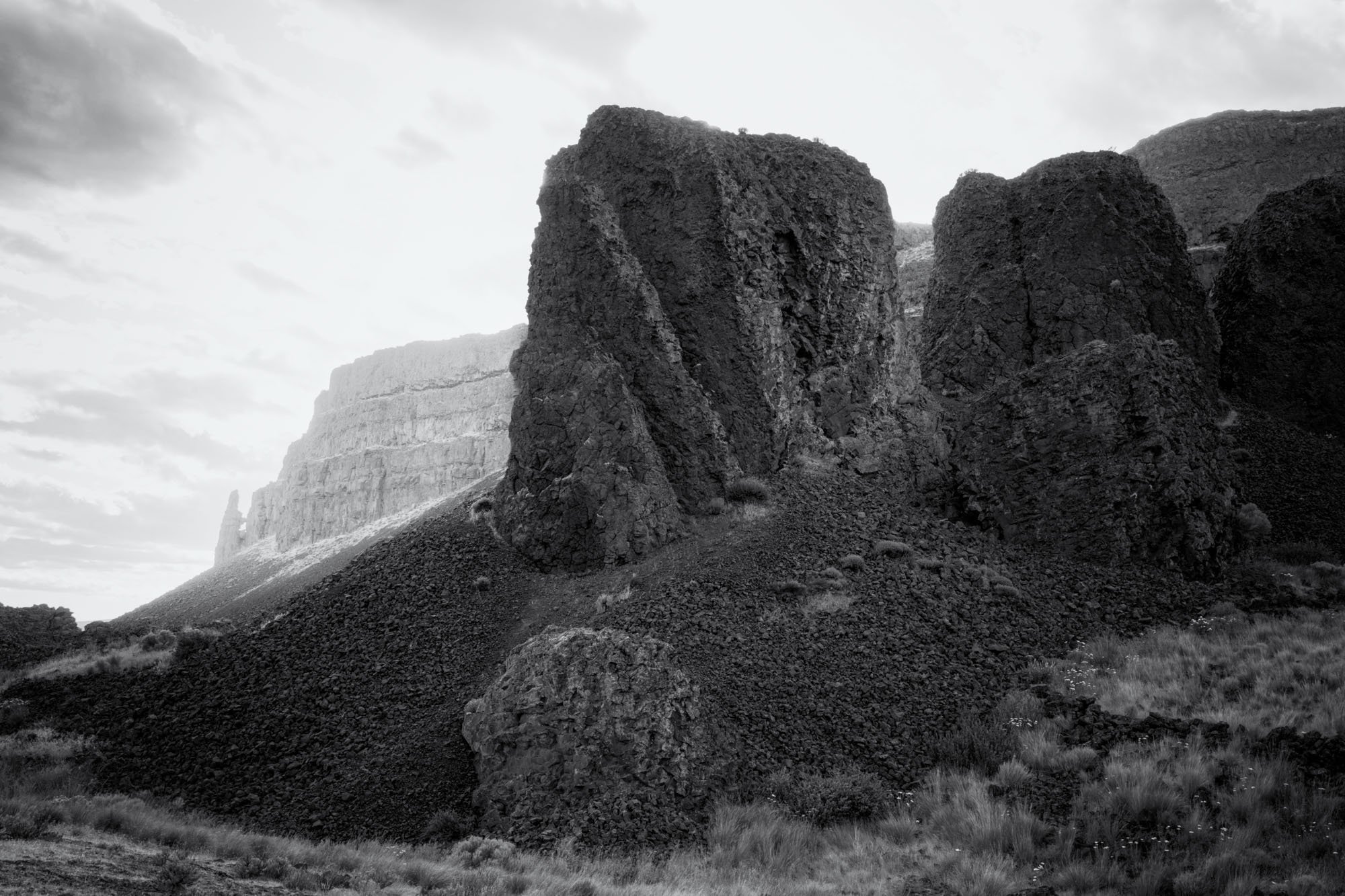 Black and white photo of large rock formations on a hillside in Eastern Washington, with a cloudy sky in the background.