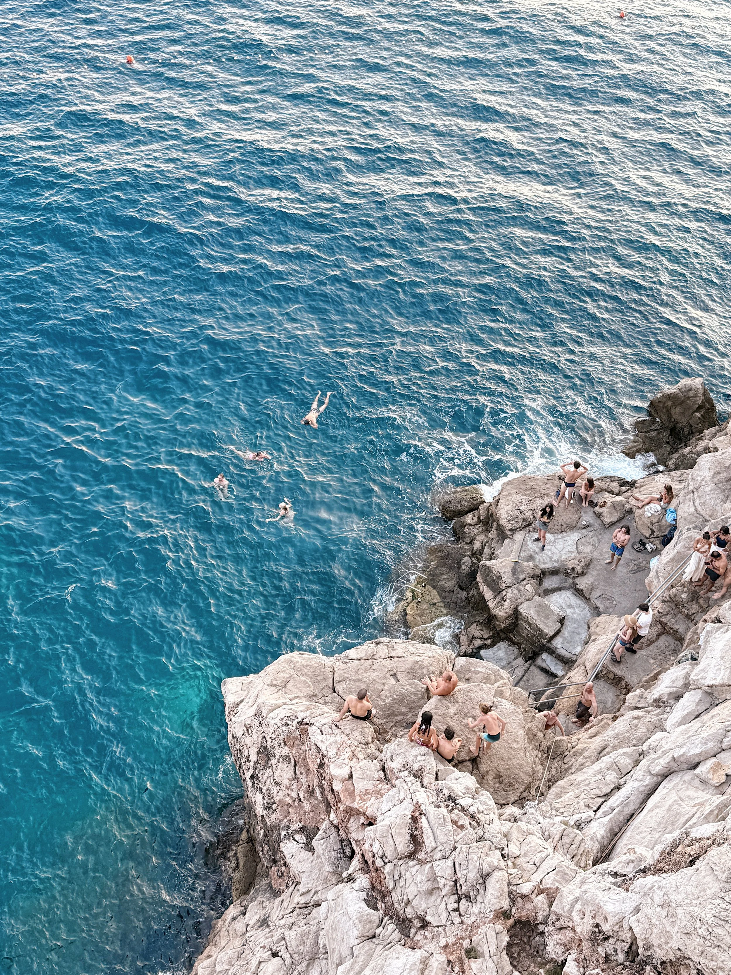 People swimming and relaxing on rocky shoreline by the ocean.