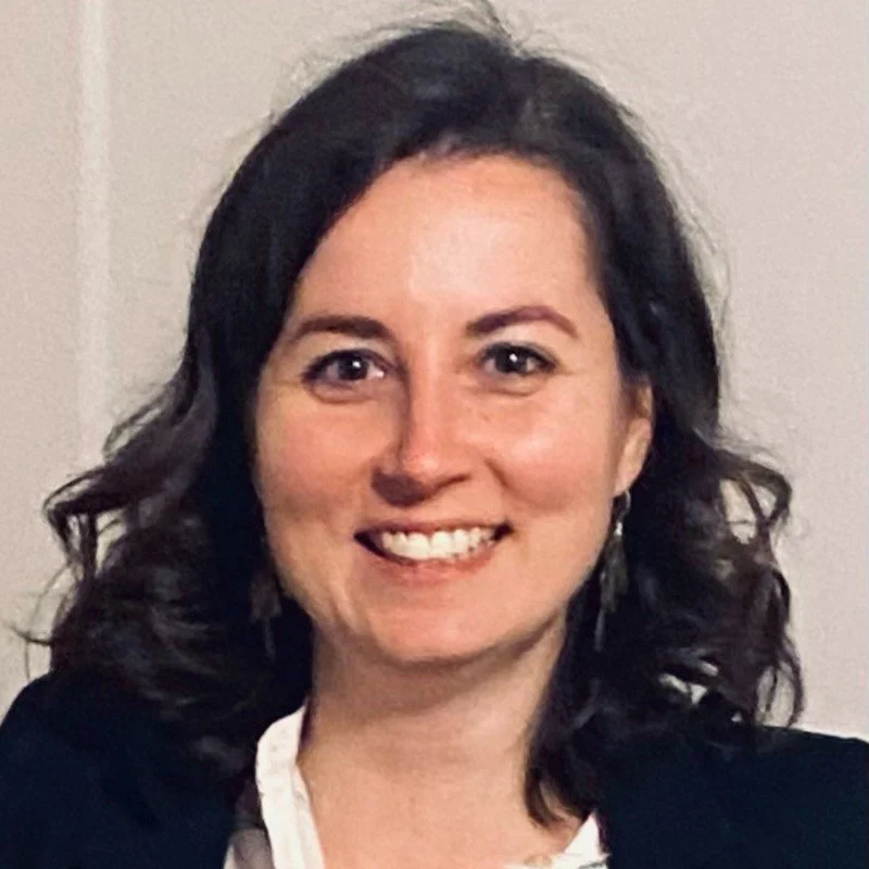 A woman in a dark suit in standing against white background.