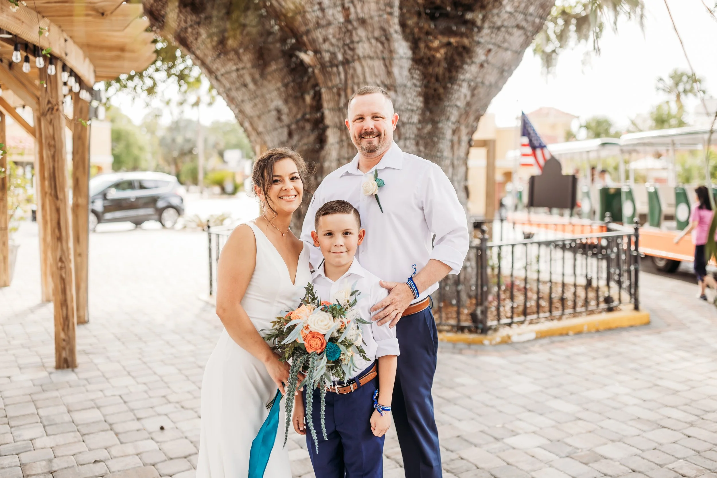 Family of three smiling together during a St. Augustine elopement, with bride holding a bouquet and child standing between parents