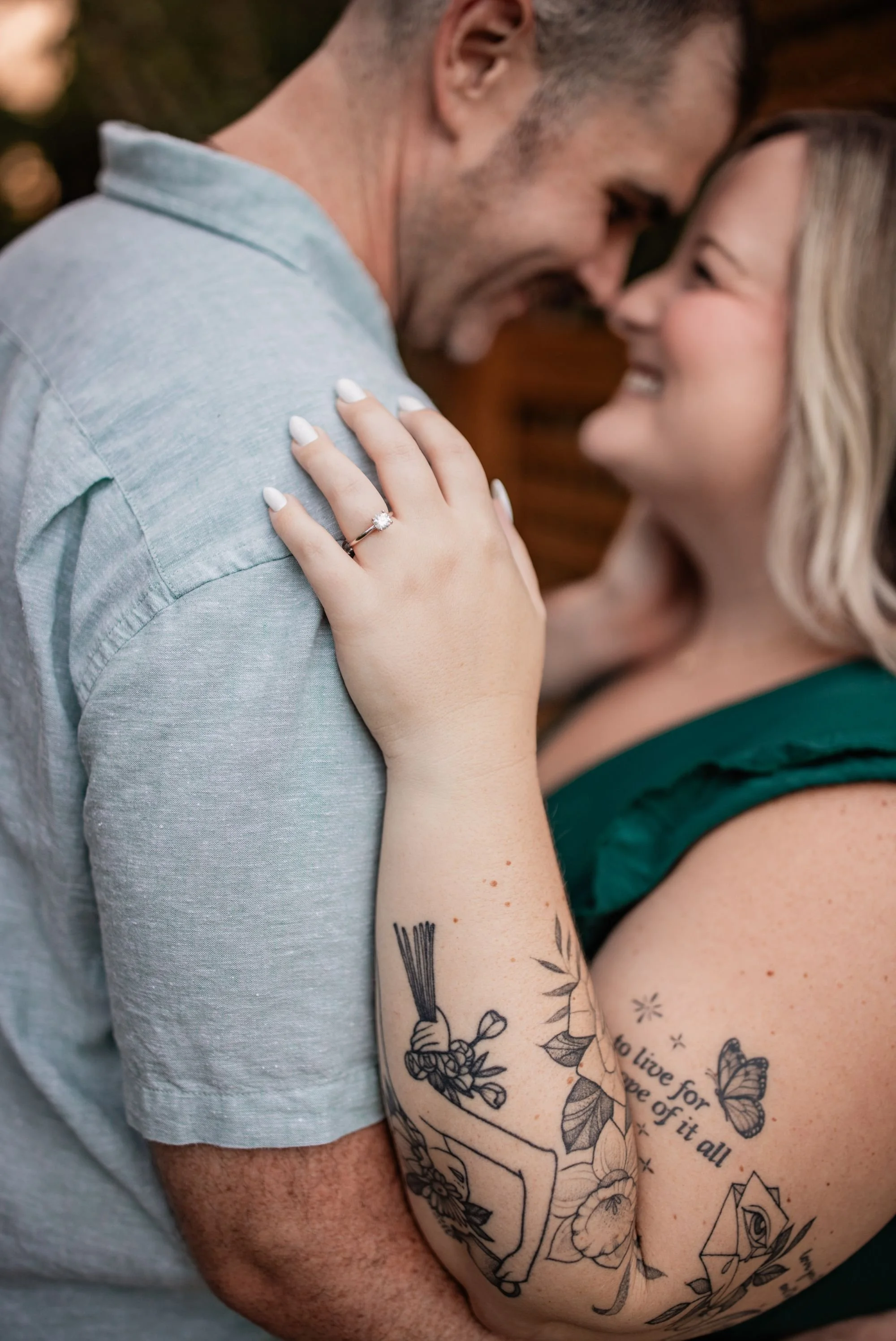 Close-up of an engagement ring with the couple smiling together in the background.