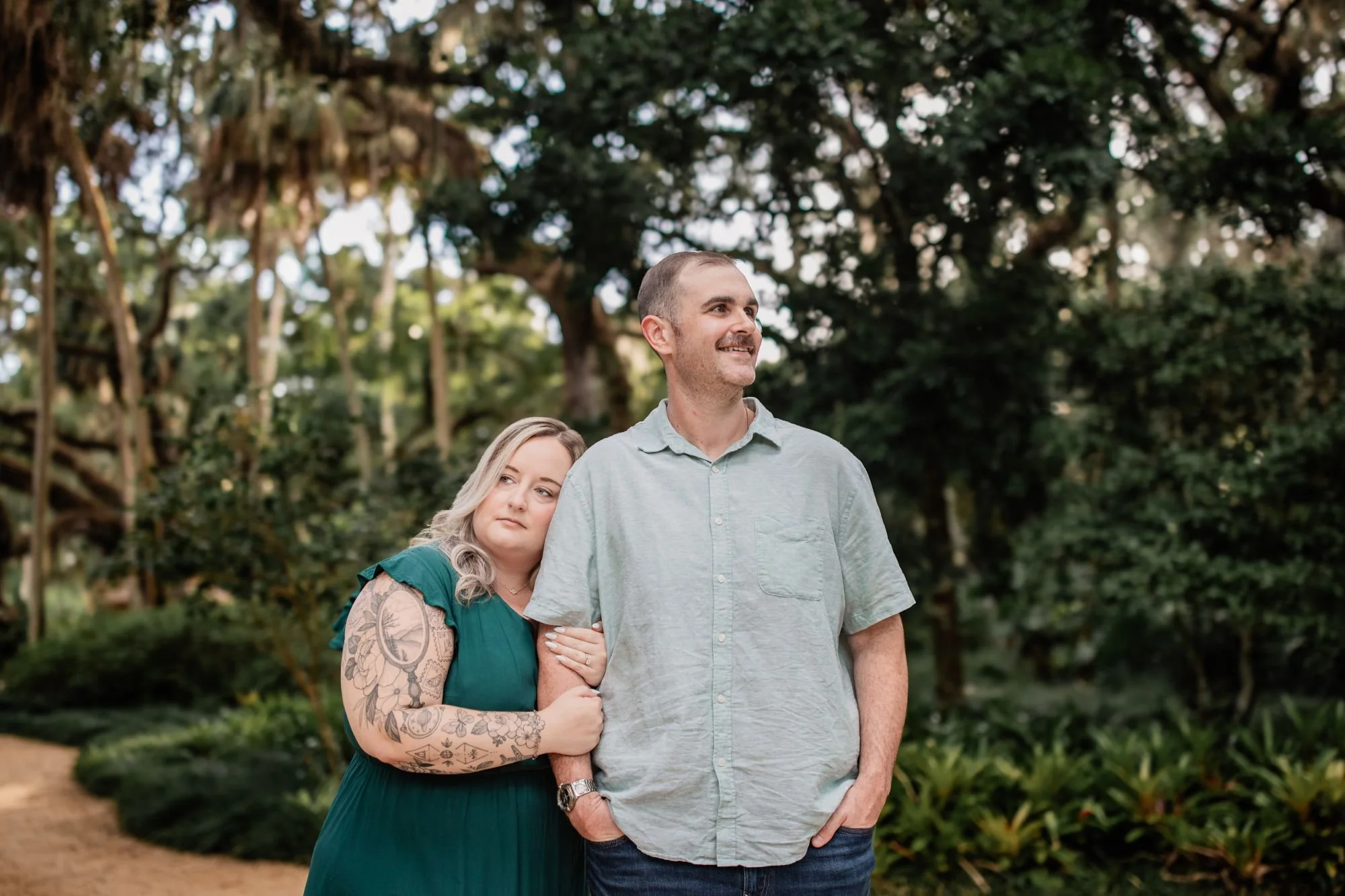 Engaged couple standing together surrounded by lush greenery and oak trees at Washington Oaks Gardens.