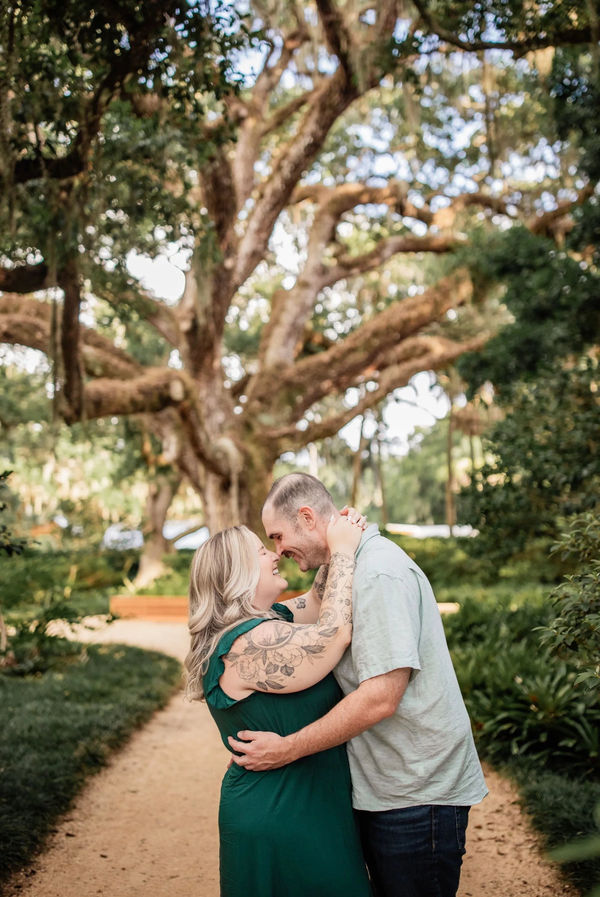 Couple laughing together beneath a sprawling oak tree during their Washington Oaks engagement session.