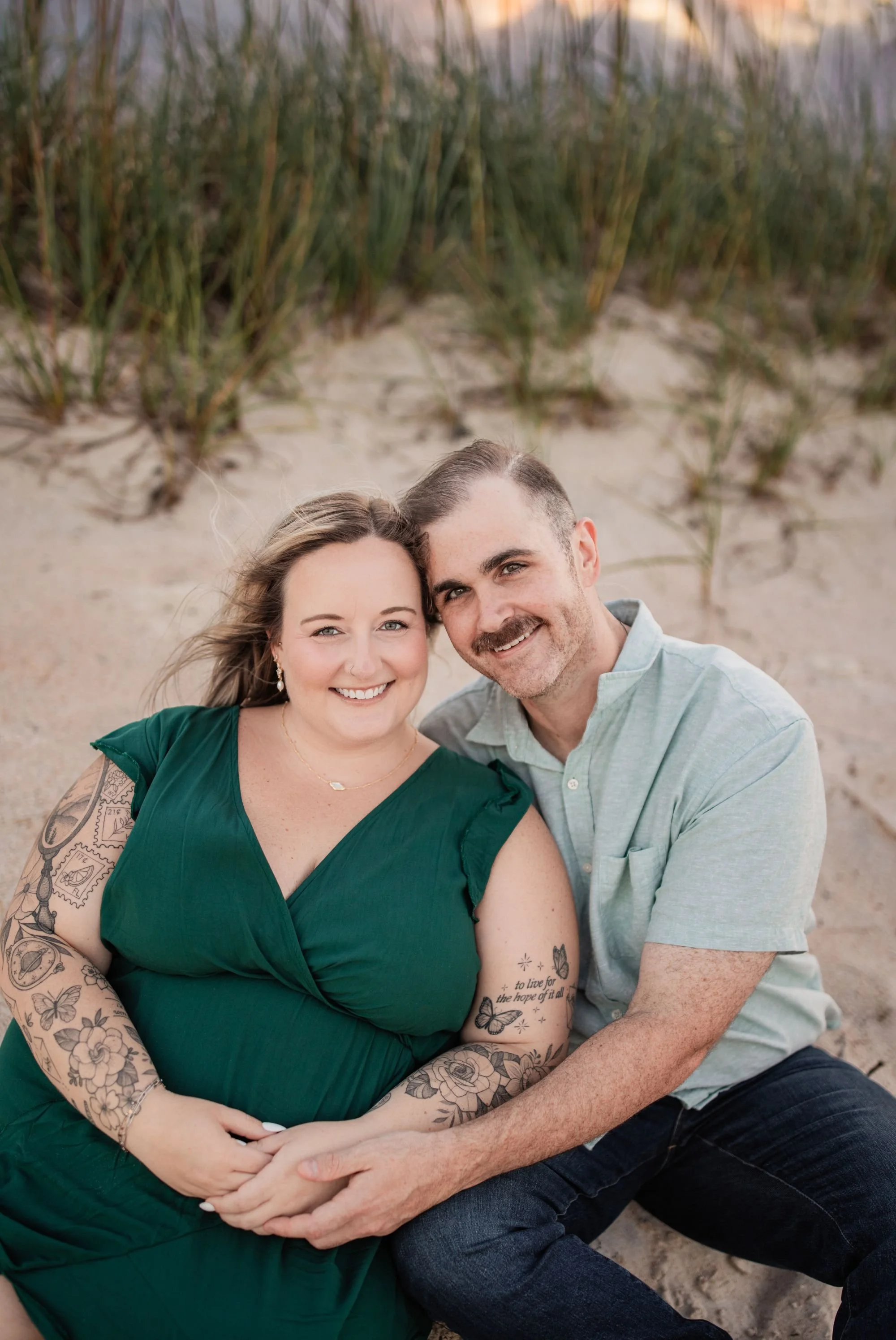 Smiling engaged couple sitting together in the sand during their Washington Oaks beach engagement session.