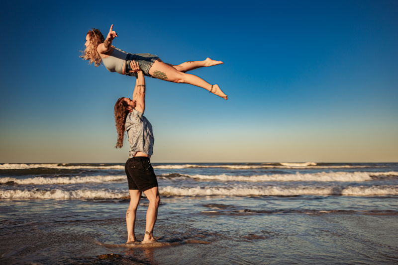 Two women laughing at the beach in relaxed blue and neutral outfits for a playful couples session
