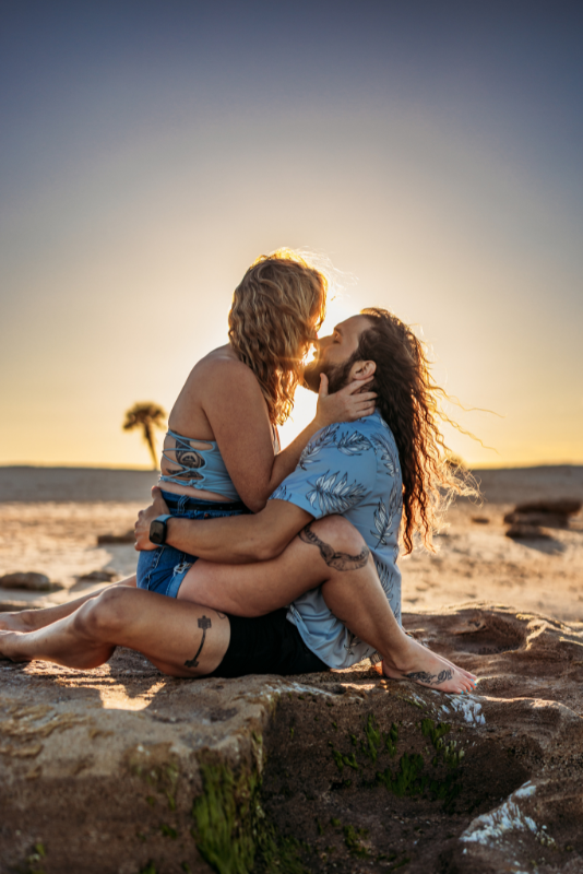 Two women kissing on coquina rocks in coordinated blue patterned outfits at sunset