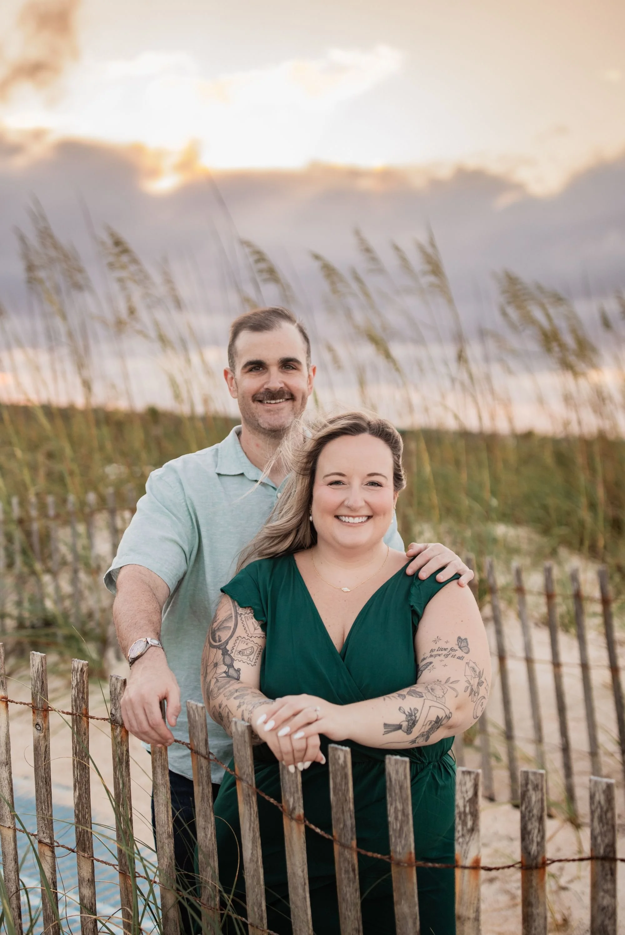 Engaged couple smiling together by the dune fence and sea oats at sunset at Washington Oaks beach.