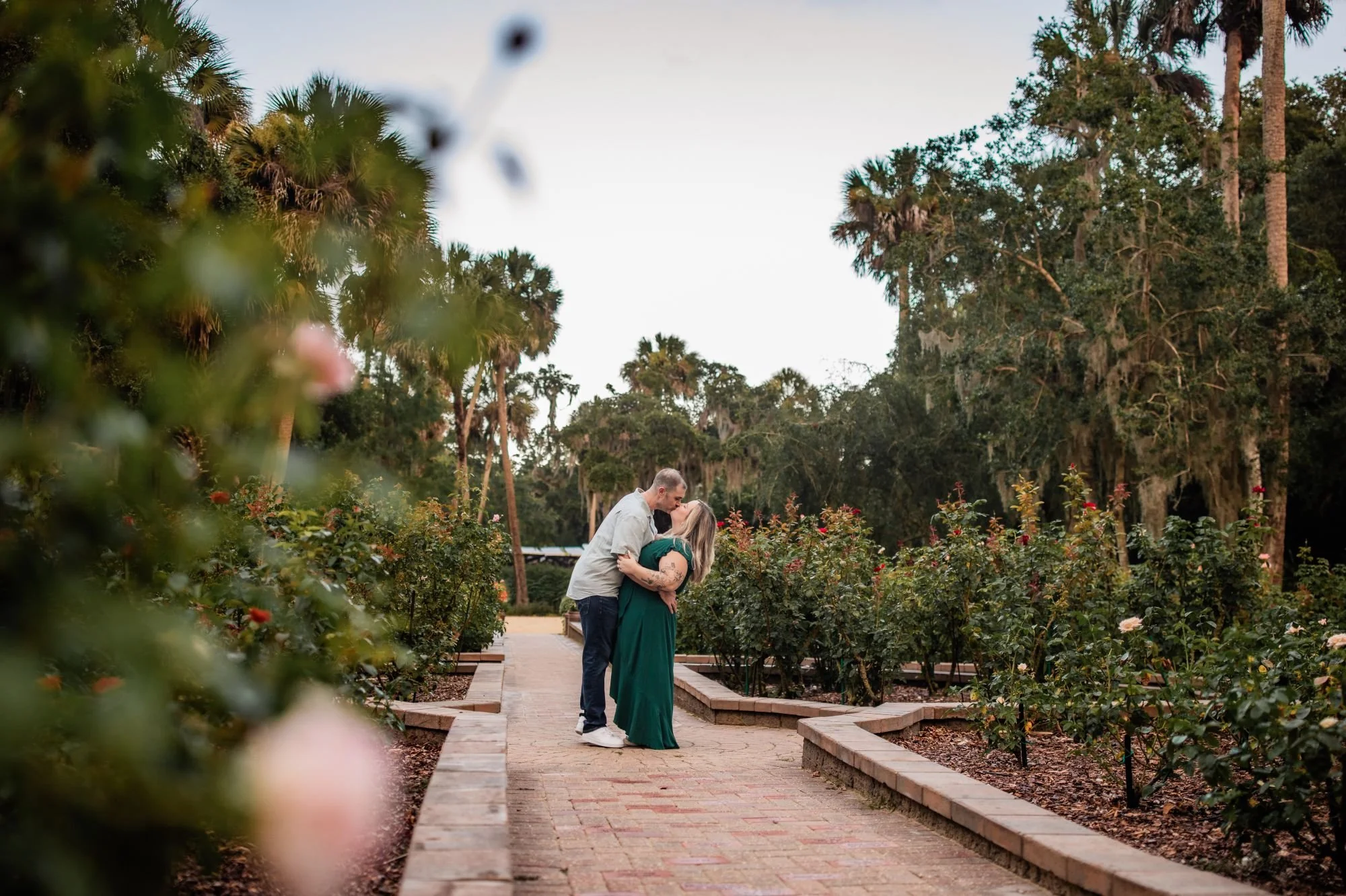 Couple kissing on a brick pathway surrounded by roses at Washington Oaks Gardens.