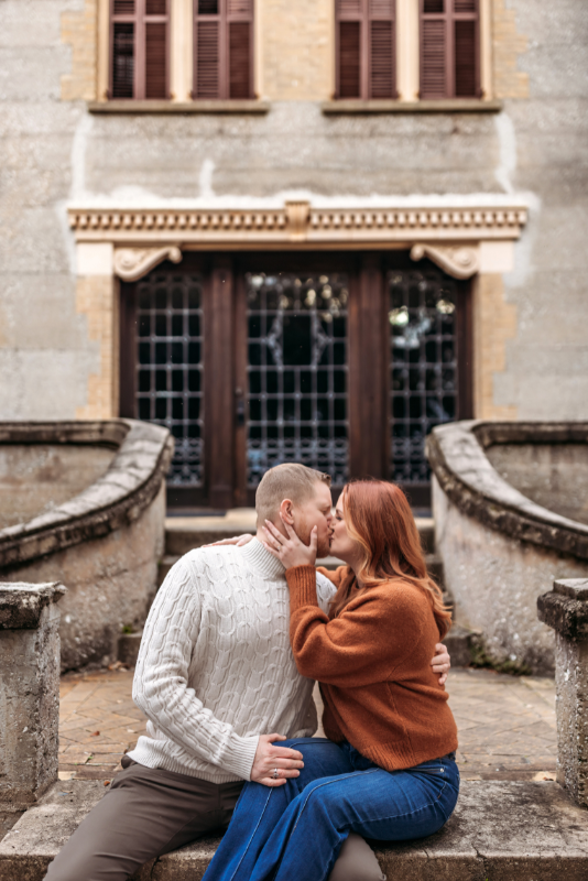 Couple kissing on historic stone steps in rust and cream sweaters for a fall photo session